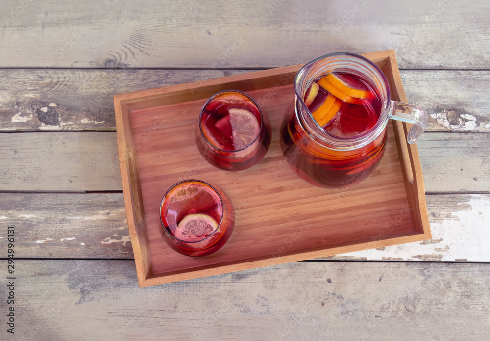 Red wine sangria with fruits in glasses and pitcher on wooden tray on rustic wooden table. Selective focus. Red wine sangria with fruits in glasses and pitcher on wooden tray on rustic wooden table. Selective focus.