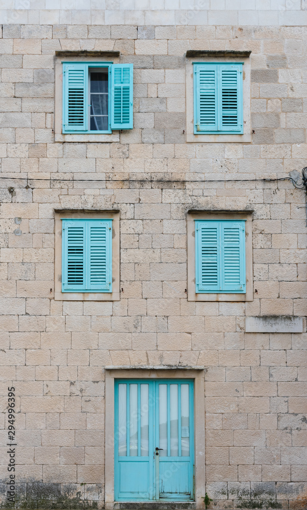 Street and front view of an old mediterranean stone house with turquoise doors and window shutters, typical mediterranean architecture, Vis island, Croatia, Europe. Summer travel concept.