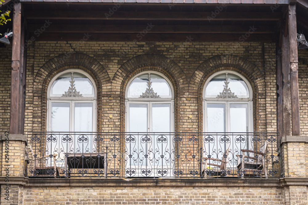 An ornate older house with a nice bright balcony with chairs and tables An ornate older house with a nice bright balcony with chairs and tables