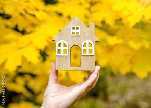 The symbol of the house in the girl's hand on the background of yellow maple leaves 