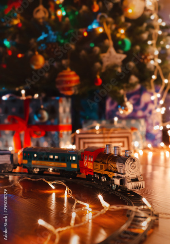 toy vintage steam locomotive on the floor under a decorated Christmas tree on a background of bokeh lights garland.