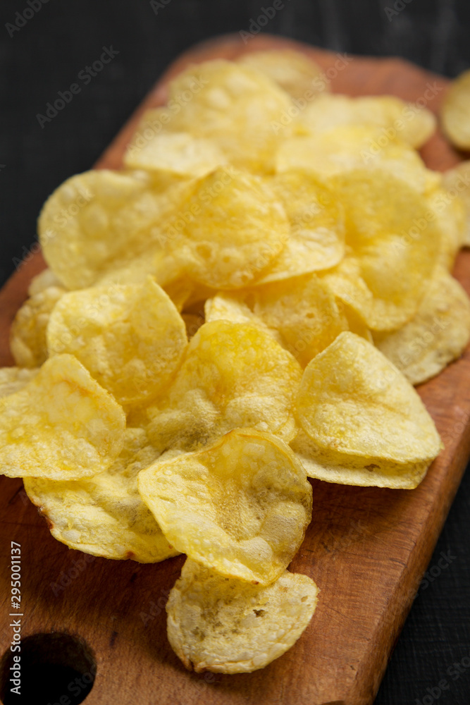 Crispy potato chips with salt on a rustic wooden board on a black surface, side view. Closeup. Crispy potato chips with salt on a rustic wooden board on a black surface, side view. Closeup.