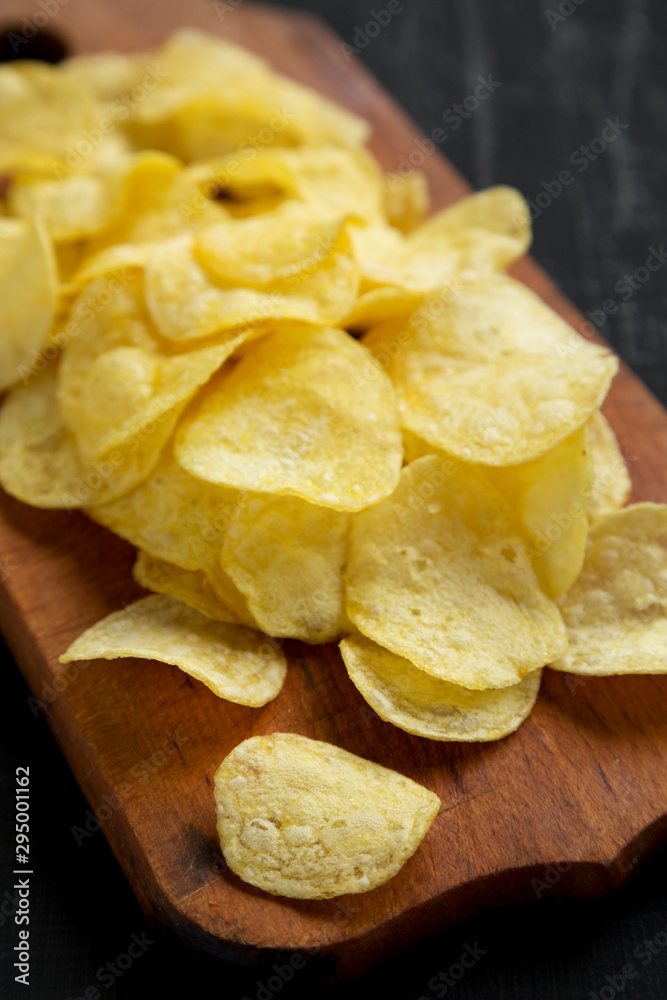Crispy potato chips with salt on a rustic wooden board on a black background, side view. Close-up.