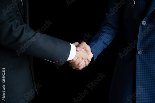The business man in a black suit and a blue suit holding hands to make business deals on a black background.