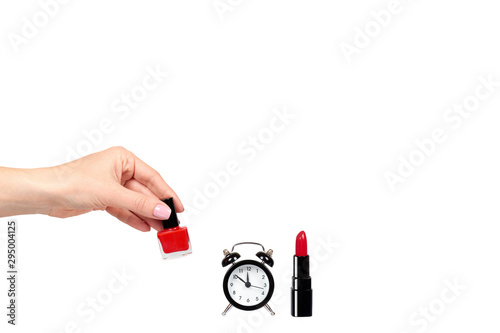 Hand with red nail polish, lipstock and alarm clock.