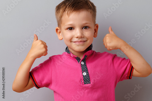 Little boy in t-shirt showing thumbs up sign over grey background
