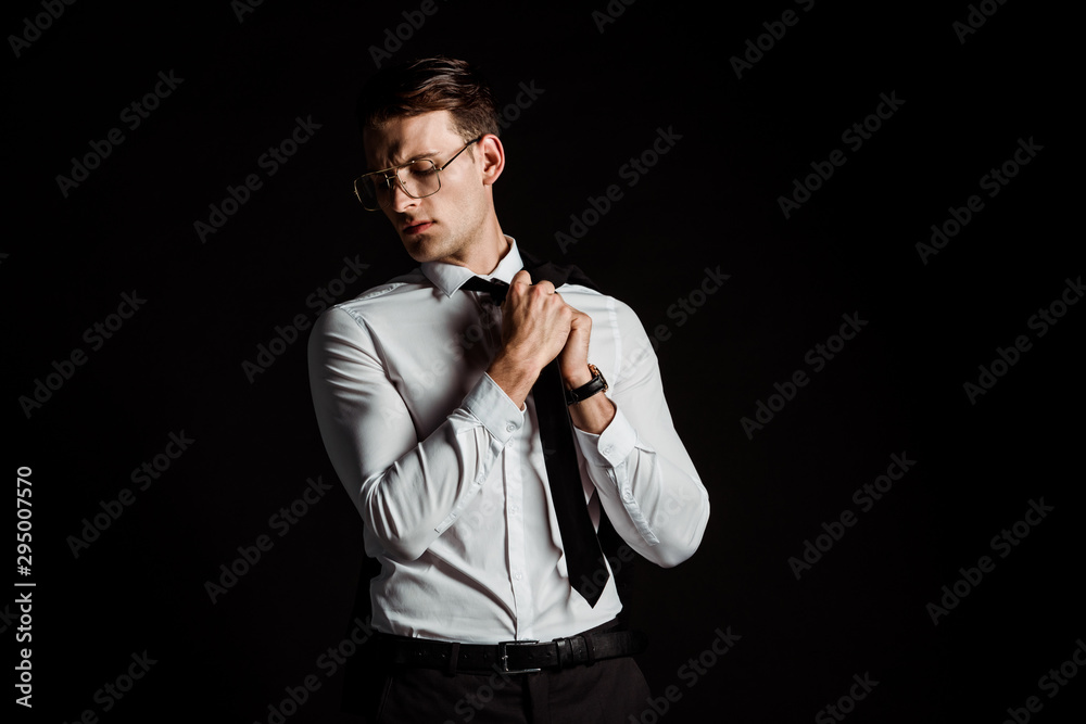 handsome businessman in glasses touching tie isolated on black handsome businessman in glasses touching tie isolated on black