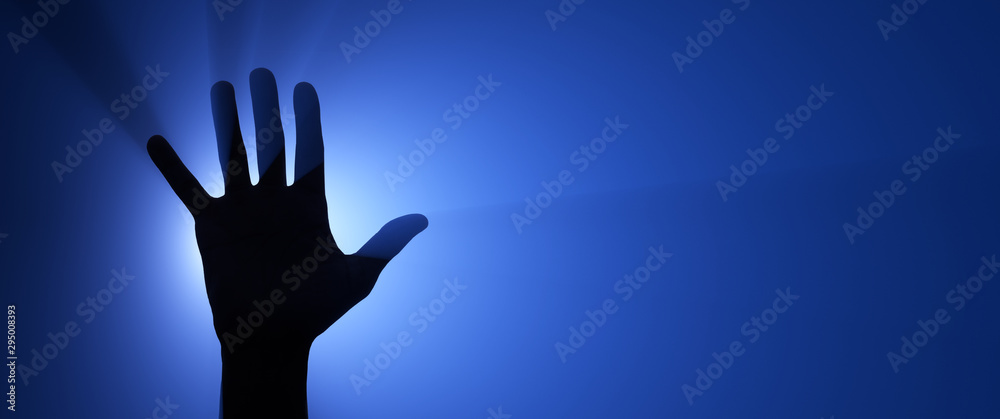 Silhouette of a raised hand. Spotlight in the background. Silhouette of a raised hand. Spotlight in the background.