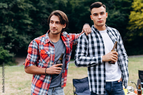 Two guys standing and holding a beer in the camping. - Image