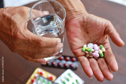 Obraz na płótnie Elderly Asian man holding many pills (tablet,capsule ) and glass of water in hands