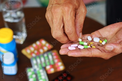 Close up at elderly Asian man holding many pills(tablet and capsule) in hands and pick some medicines for taking supplements antibiotic,antidepressant or painkiller medication Hope for cure.