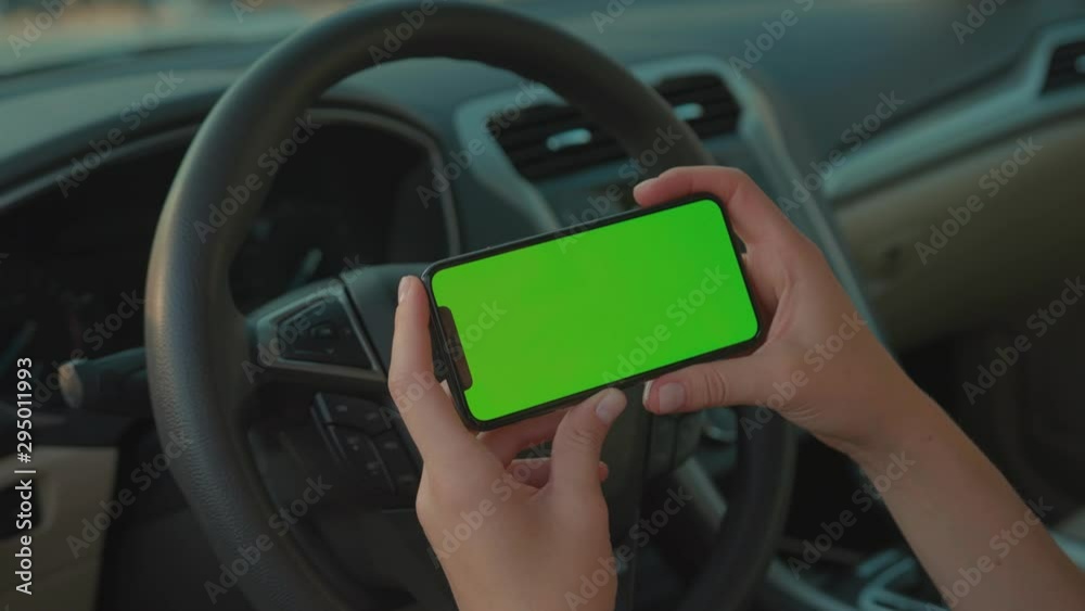 Handheld shot of young woman driver sitting inside car using horizontal smartphone mobile application on driver seat. People and technology. Handheld shot of young woman driver sitting inside car using horizontal smartphone mobile application on driver seat. People and technology.