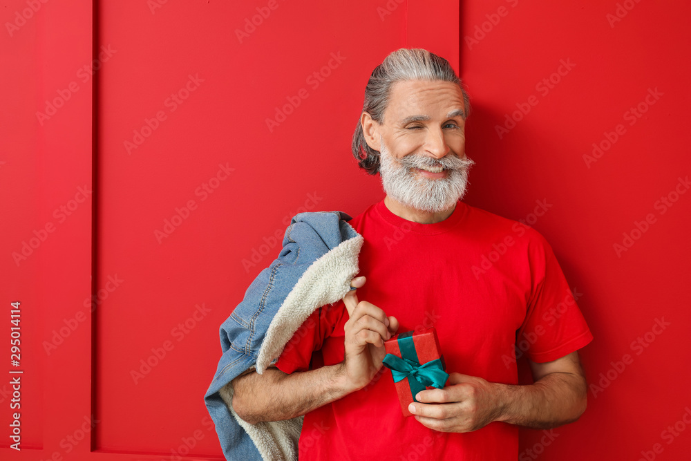 Portrait of stylish Santa Claus with Christmas box on color background