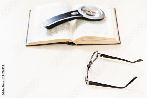 spectacles and magnifying glass on open book