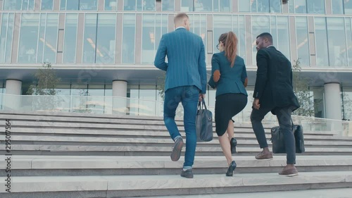 Confident team members walking on stairs in slow motion. Business men and woman in formal suits go and talk on the background of modern office building