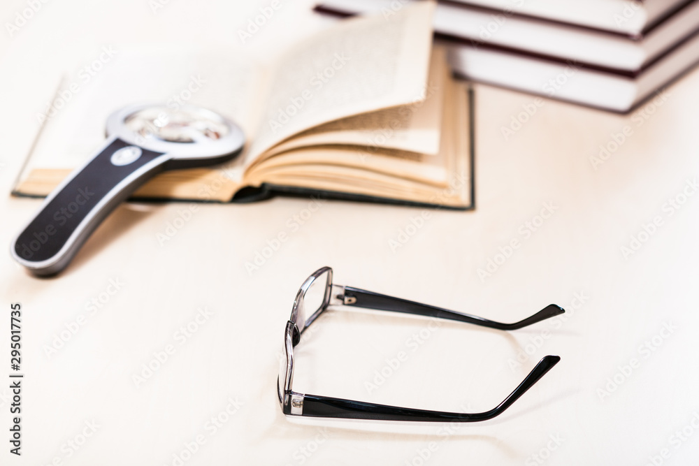 eyeglasses and magnifier near stack of books eyeglasses and magnifier near stack of books