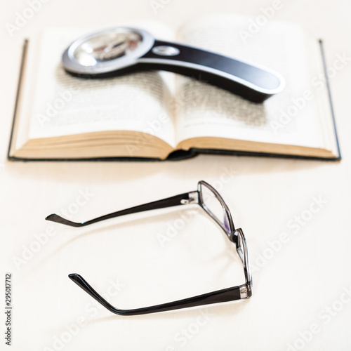 spectacles and loupe on open book on pale table