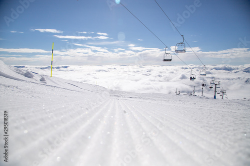 Snow velvet on ski slope on the background of snowy mountain peaks. Prepared ski and snowboard track with trace of snow groomer on snow.