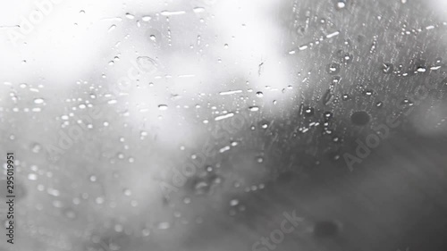 Close up on windshield on a rainy day. The raindrops fall and the wipers brush them away. There is condensation on the window, making it steamed up and foggy. The rain droplets spread as they hit.