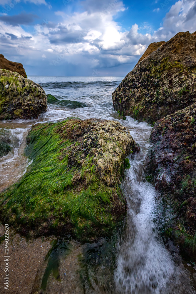 Beautiful seascape with a close view of stones with moss and flowing water between. Vertical view