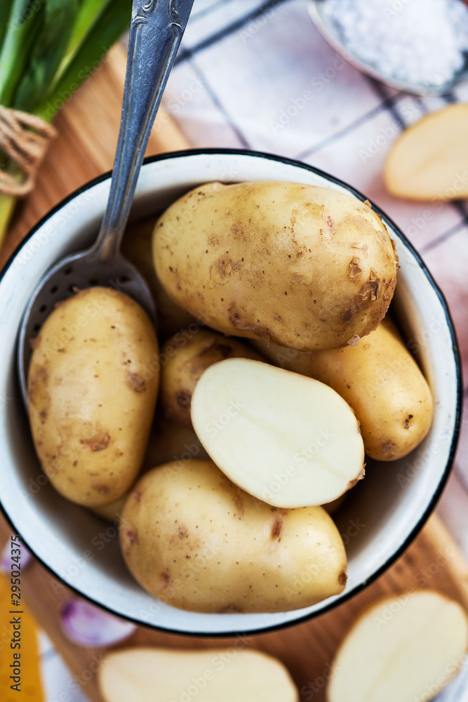 raw potatoes in an enameled bowl with a spoon on a yellow background with a kitchen towel raw potatoes in an enameled bowl with a spoon on a yellow background with a kitchen towel