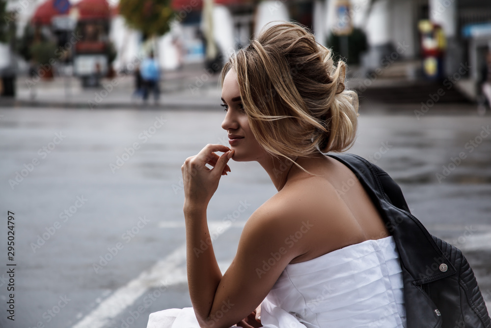 Portrait of style woman sit on a road , elegant model wearing wedding dress and holding black leather jacket.