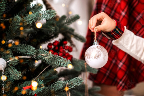 Little child's hand decorating Christmas tree indoors.