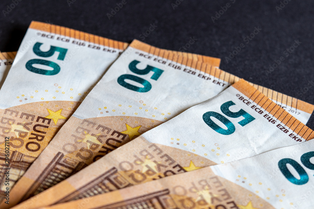 View of several fifty Euro banknotes in different arrangements against black background View of several fifty Euro banknotes in different arrangements against black background