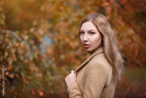 portrait of a young beautiful woman blonde girl in a beige coat on the background of autumn Park