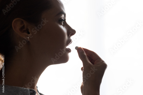 side view of beautiful woman taking pill at home