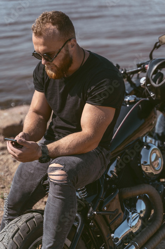 Handsome bearded man sitting on bike while looking at the phone