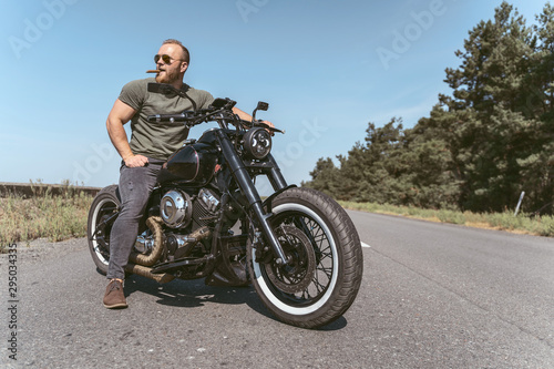 Handsome serious biker sitting on bike on the road
