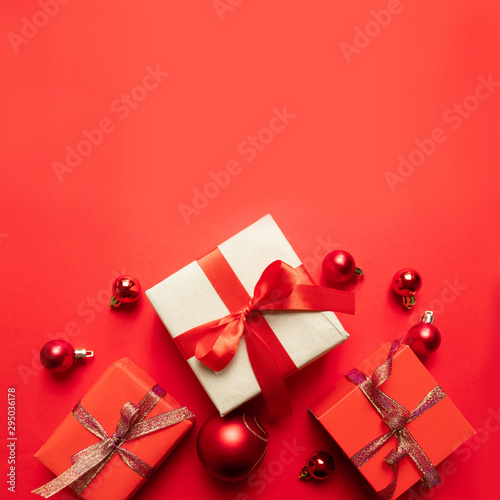 Creative Christmas composition with red present box, ribbons, red big and small balls, holiday decorations on red background. Flat lay, top view, copy space