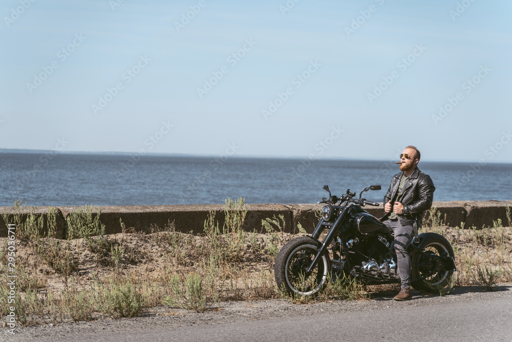 Obraz premium Sexy man in leather jacket sitting on bike by the ocean