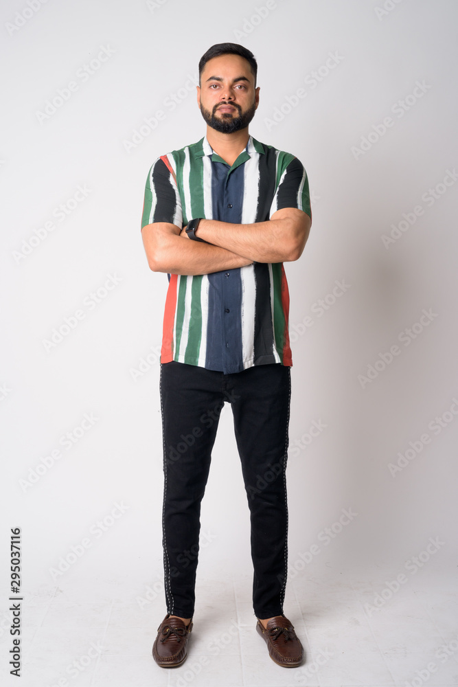 Full body shot of young bearded Indian man with arms crossed