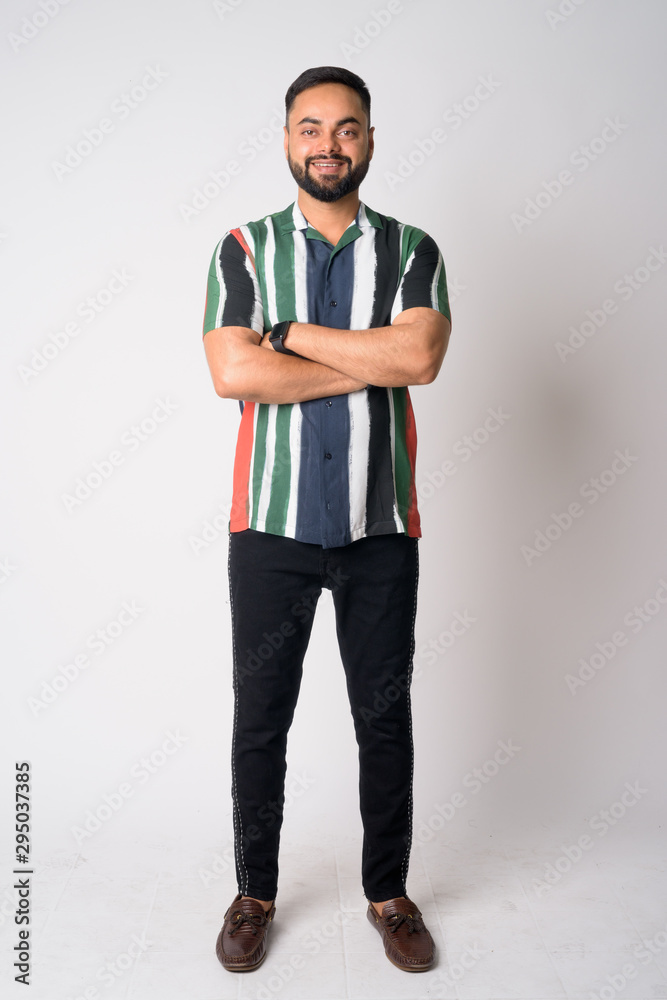 Full body shot of happy young bearded Indian man smiling with arms crossed Full body shot of happy young bearded Indian man smiling with arms crossed