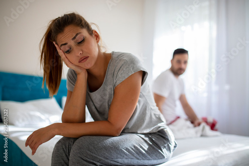 Couple in conflict standing sad in the bed. Stressed couple arguing and having marriage problems. Young couple having problems. Woman and man having a disagreement, Young couple in a bed bored woman photo