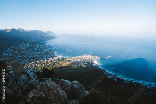 The view from on top of Table Mountain, Cape Town, South Africa. Beautiful mountainous landscape with the sea and iconic bays in the distance. The golden sun is setting over the ocean horizon. 
