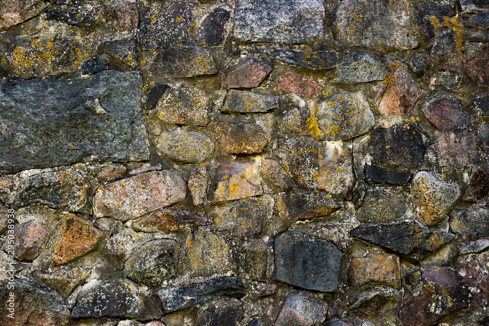 Weathered stone wall of large cobblestones overgrown with moss
