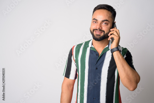 Portrait of happy young bearded Indian man talking on the phone