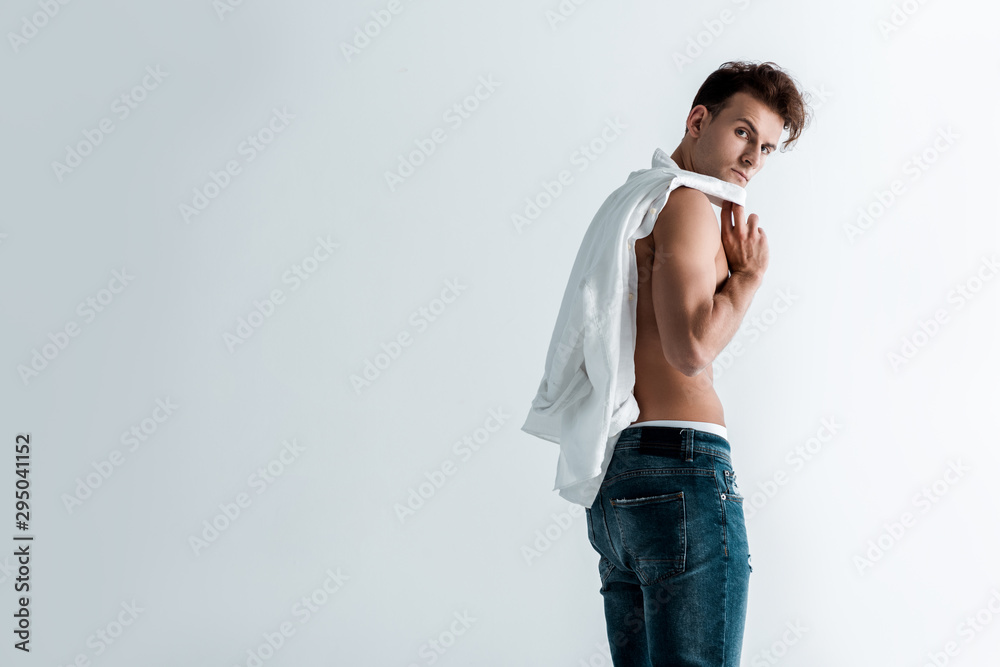 muscular young man in denim jeans standing and holding shirt on white muscular young man in denim jeans standing and holding shirt on white