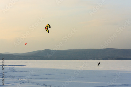 snowkiting the athlete in equipment controls the kite and extreme snowboarding on a huge mountain lake. fresh clean snow and frosty landscape. wild nature background