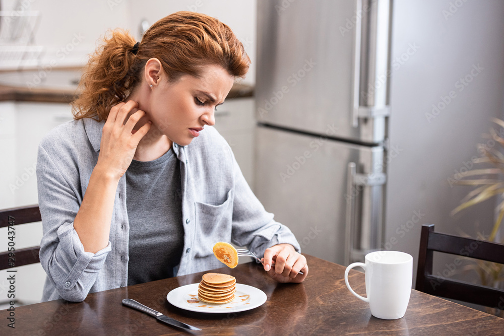 attractive woman with allergy scratching neck while holding fork with pancake attractive woman with allergy scratching neck while holding fork with pancake
