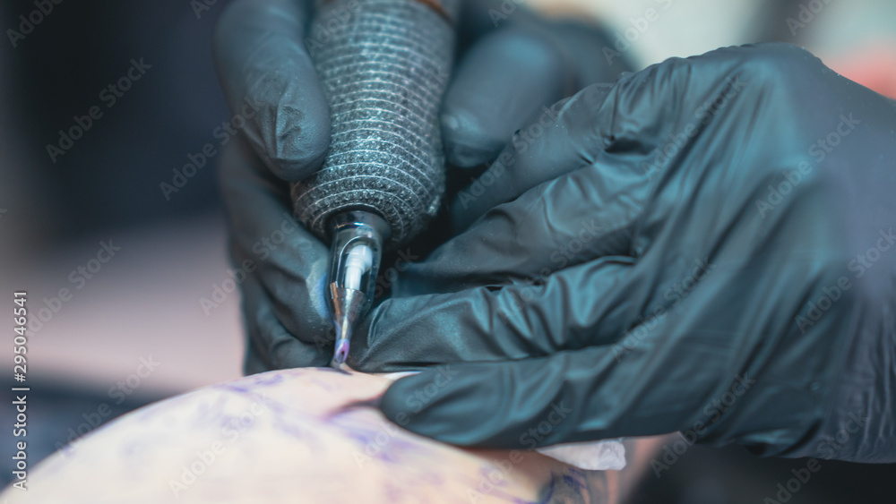 Professional tattoo artist makes a tattoo on a young man’s hand, close-up. Tattoo artist doing tattoo in tattoo salon.