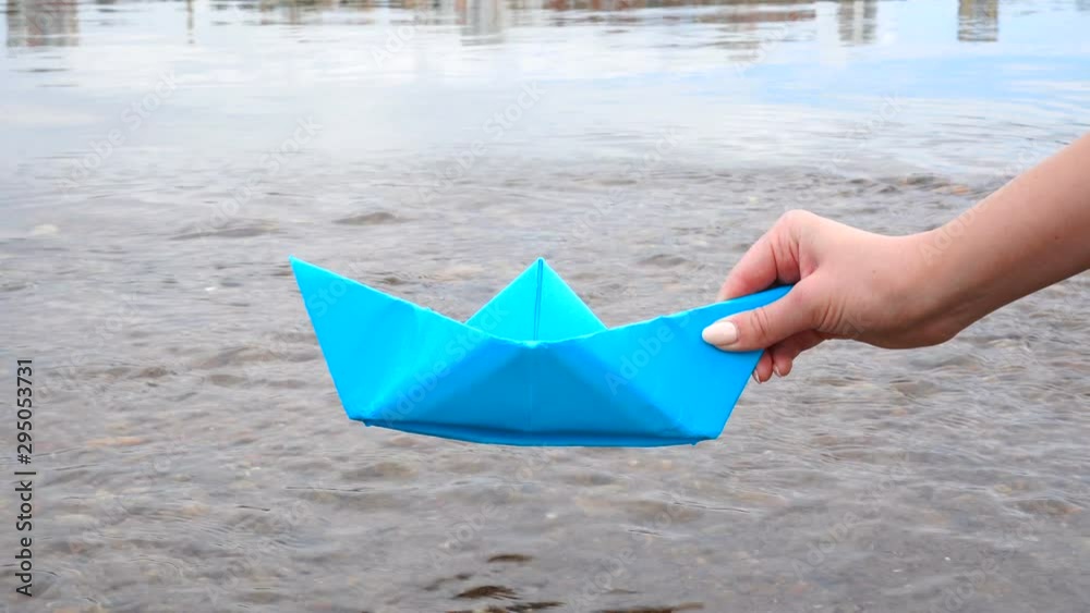 Woman's hand holding blue paper boat over the river Woman's hand holding blue paper boat over the river