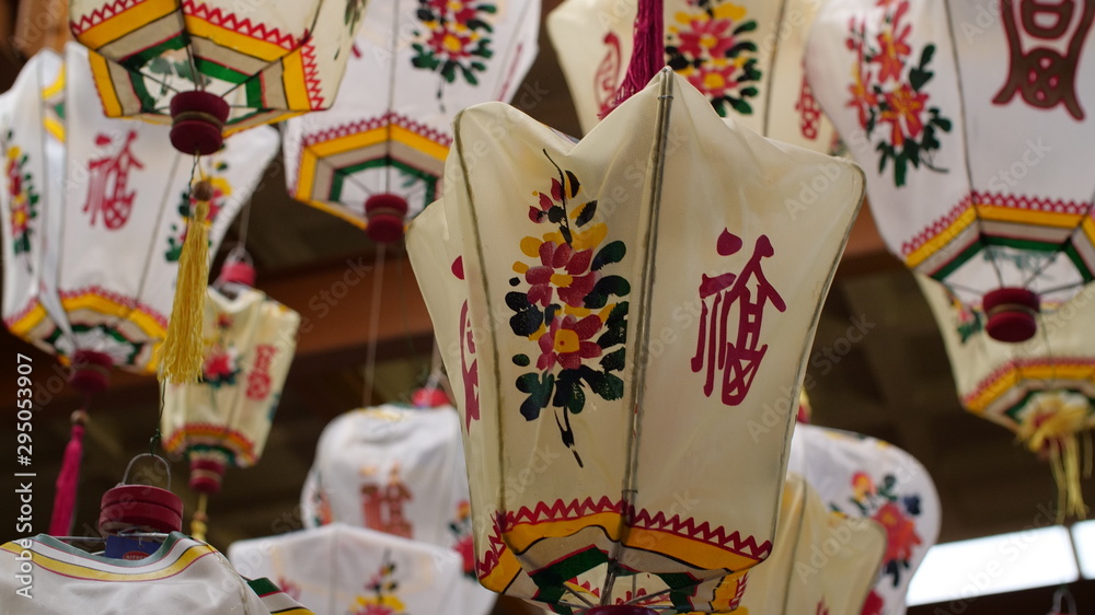 Obraz premium A group of old traditional Chinese lanterns hangs in a dusty antique warehouse, they're full of the beautiful script, colour & patterns. 