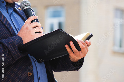 Obraz na plátně A preacher with a microphone in his hand holds a Bible and reads a passage from