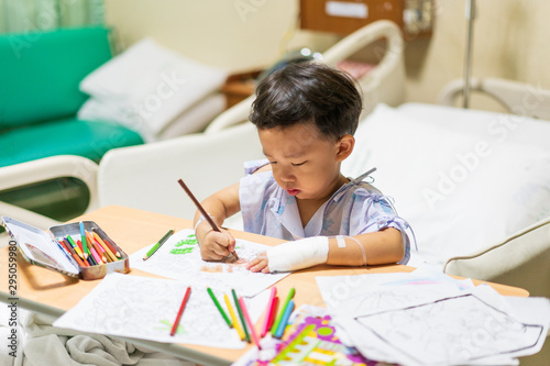 The patient boy is painting the paper with a color pencil in the hospital.