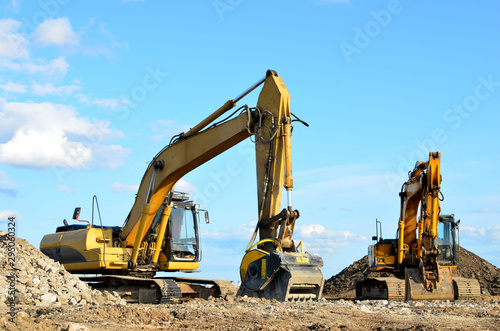 Two yellow excavators at a construction site. Excavator with crusher bucket for crushing concrete. Construction waste recycling for construction mix. Sifting, grinding and separation of concrete