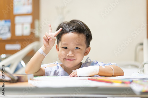 The patient boy is painting the paper with a color pencil in the hospital.